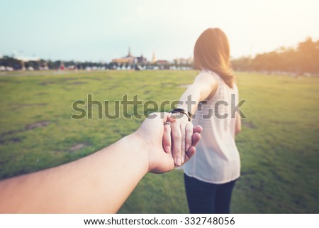 Young woman holding man hand on the greenfield. Focus on hands. traveller, vintage processed.