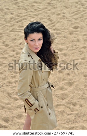 Beautiful young girl stands in a coat on the sand in windy weather