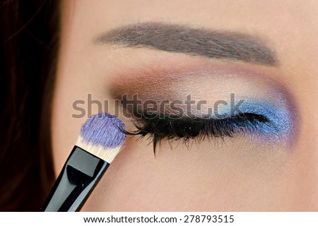 Portrait of sexy fashion model girl with perfect bright eye makeup. Beautiful woman with long false eyelashes. Close-up of a closed eye with blue and purple color shadows. Brush of a makeup artist