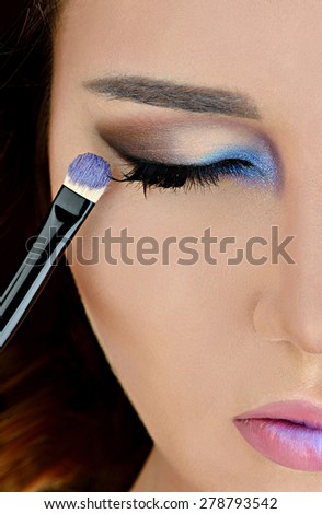 Portrait of sexy fashion model girl with perfect bright makeup. Beautiful woman with shiny pink lipstick. Close-up of an eye with blue and purple color shadows. Brush of a makeup artist. Glossy lips
