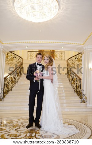 Beautiful sexy model girl in white dress. Wedding couple. Man in suit. Beauty blonde bride with brunette groom. Female and male portrait with bouquet. Woman with lace veil. Cute lady and guy indoors