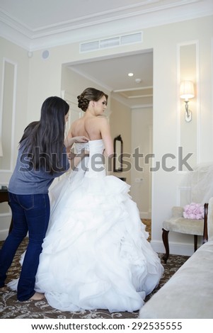 Bridesmaid is lacing white wedding dress for beautiful bride. Beauty model girl in bridal gown for marriage. Female portrait. Woman with curly hair and lace veil. Cute lady indoors