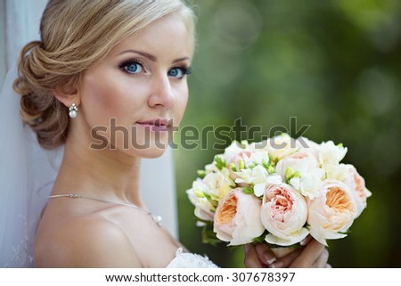 Beauty bride in bridal gown with bouquet and lace veil on the nature. Beautiful model girl in a white wedding dress. Female portrait in the park. Woman with hairstyle. Cute lady outdoors
