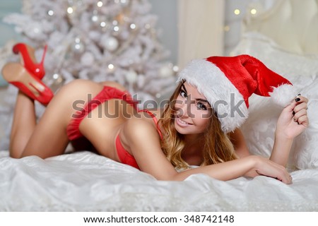 Beautiful sexy Santa Clause in elegant panties, hat and bra. Fashion portrait of model girl indoors with christmas tree. Cute woman in lace red lingerie. Female ass in underwear. Naked body
