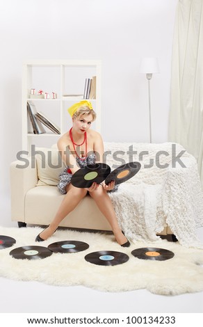 indoor portrait of beautiful young blonde size plus woman model sitting on sofa choicing one of two vinyl records in hands