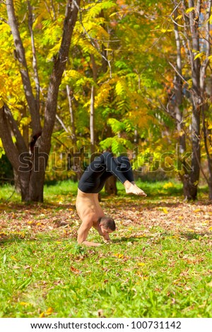 Man exercises in the autumn forest yoga vrishchikasana pose