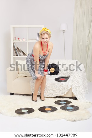 indoor portrait of beautiful young blonde size plus woman model standing on fur carpet with vinyl records around in interior