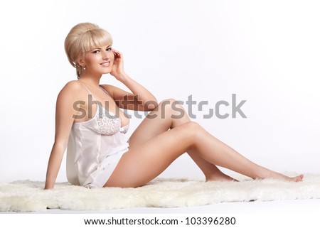 full-length portrait of beautiful young blonde woman in lingerie sitting on white fur carpet