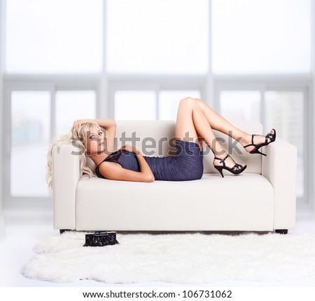 full-length portrait of beautiful young blond woman on couch with white furs on floor