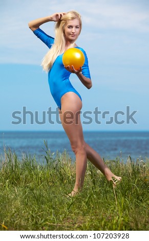 outdoor portrait of young beautiful blonde woman gymnast exercising with ball on grass