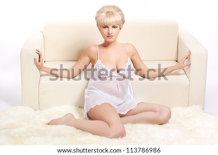 full-length portrait of beautiful young blonde woman in lingerie sitting near white sofa