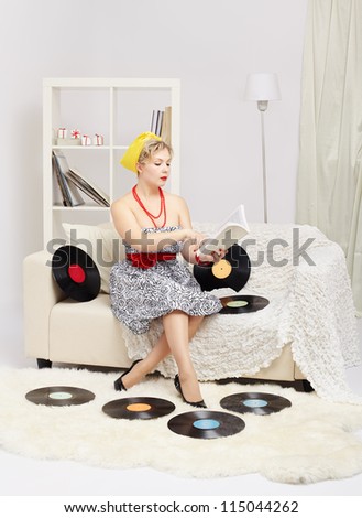 indoor portrait of beautiful young blonde size plus woman model sitting on sofa with vinyl records around and reading book