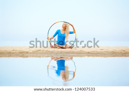 outdoor portrait of young beautiful blonde woman gymnast working out with hoop on the sand