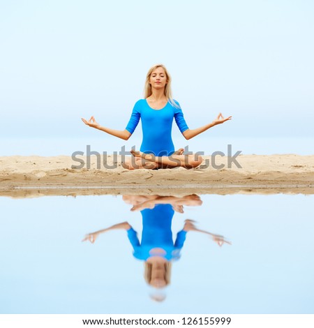 outdoor portrait of young beautiful blonde woman gymnast sitting in yoga lotus pose on the beach
