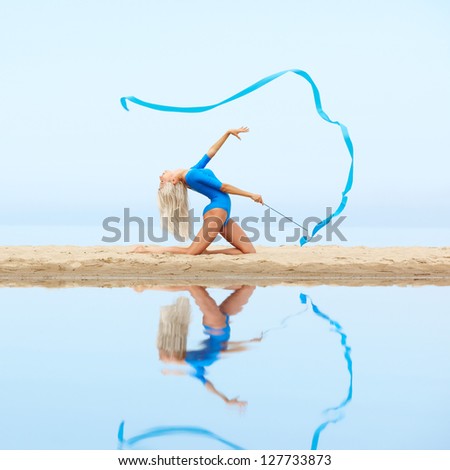 outdoor portrait of young beautiful blonde woman gymnast exercising with ribbon on the beach