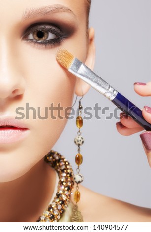 close-up portrait of beautiful young brunette woman applying eye-zone make-up with cosmetic brush