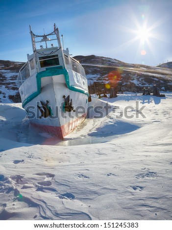Ship at moorage in frozen baikal lake at winter under Sun rays