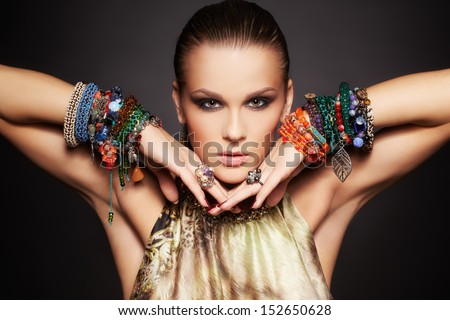 Portrait Of Beautiful Young Brunette Woman Posing In Rings And Multiple Bracelets On Dark Gray