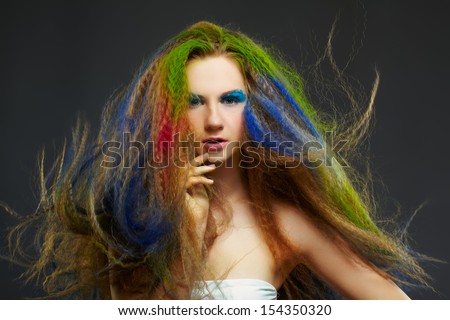 portrait of young beautiful redhead woman psoing on gray with long hair colored with green blue and red
