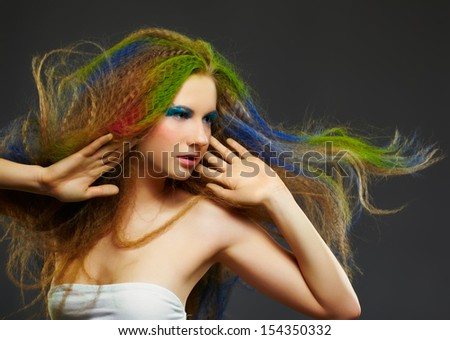 portrait of young beautiful redhead woman posing on gray with long hair colored with green red and blue