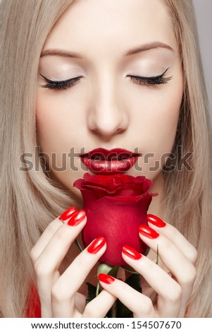 portrait of young beautiful blonde woman closing eyes and holding red rose flower in manicured hands