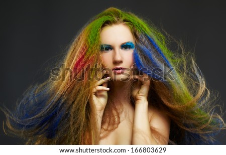 portrait of young beautiful redhead woman psoing on gray with long hair colored with green red and blue
