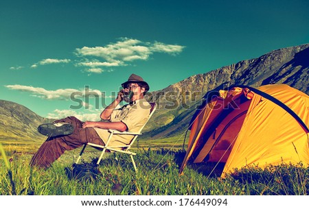 Colorized vintage outdoor portrait of tourist in Altai camp drinking tea near tent and river