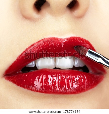 Close-up shot of woman face and makeup brush  applying red lipstick make-up on lips