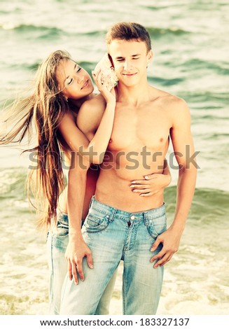 Colorized vintage outdoor portrait of beautiful topless girl putting shell to muscular guy\'s ear