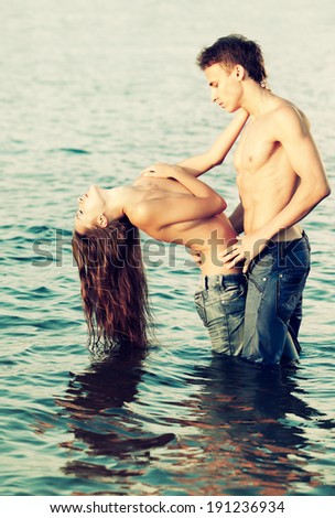 Colorized vintage outdoor portrait of  beautiful romantic couple of topless girl and muscular guy in jeans posing in sea waters