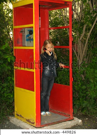 Little girl in the old public call-box with mobile phone