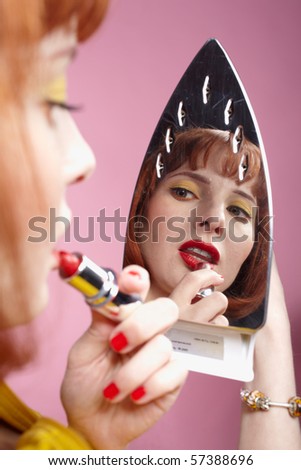 portrait of redhead woman looking at her reflection in iron and checking in her make-up