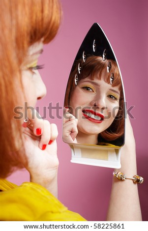 portrait of redhead woman looking at her reflection in iron and checking in her make-up
