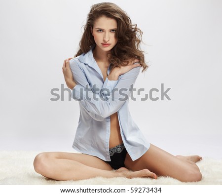 portrait of beautiful caucasian model posing on white furs in blue shirt and lingerie