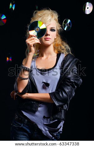 potrait of beautiful blonde girl rocker in leather jacket hiding her right eye-zone behind the cd disc. multiple shiny cds on dark background.