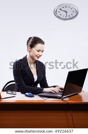 office portrait of beautiful young business woman sitting at her workplace with two laptops on gray