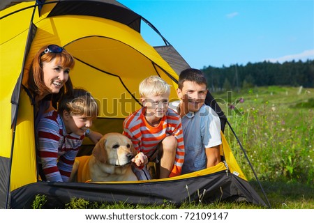 family outdoor portrait of smiling mother, two boys, young man and labrador looking happy outside of tent