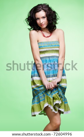 portrait of beautiful curly brunette girl in summer dress posing on green