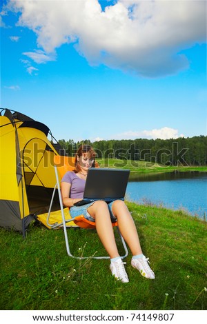outdoor portrait of beautiful woman with laptop sitting in folding chair near camp tent