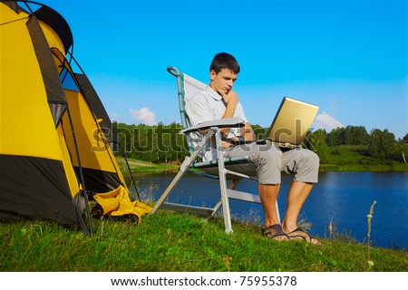 expression portrait of thoughtful man with laptop sitting in folding chair near camp tent outdoors