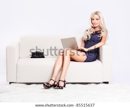 full-length portrait of beautiful young blond woman sitting on couch with laptop on her knees