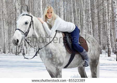 outdoor portrait of beautiful blonde girl sitting on pale horse in sunny winter forest
