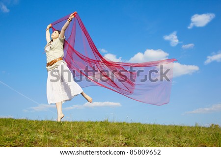 outdoor portrait of beautiful hippie girl jumping with big piece of red light cloth under the blue sky