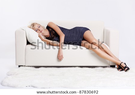 full-length portrait of beautiful young blond woman sleeping on couch with white furs on floor