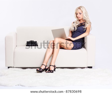 full-length portrait of beautiful young blond woman sitting on couch with laptop on her knees