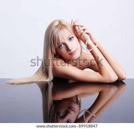 portrait of young beautiful long-haired blonde woman sitting with pearls at reflecting table