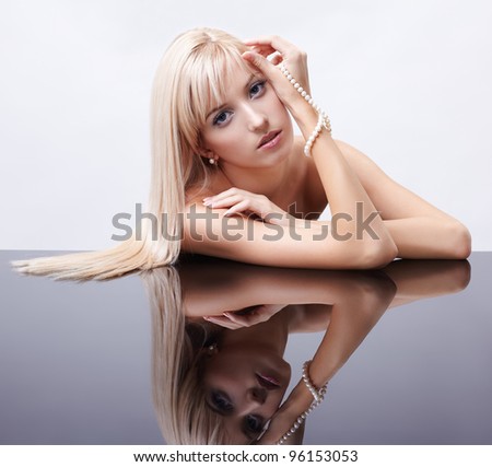 portrait of young beautiful long-haired blonde woman sitting with pearls at mirror table