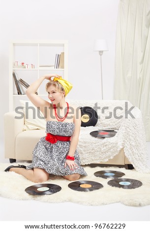indoor portrait of beautiful smiling young blonde size plus woman model sitting on fur carpet with vinyl records around in interior