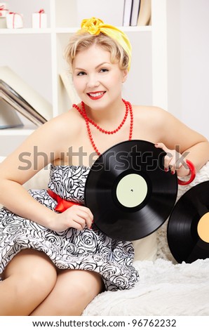 interior portrait of beautiful young happy blonde size plus woman model sitting on sofa with vinyl records