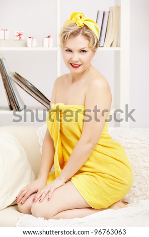 interior portrait of beautiful young blonde size plus woman model in yellow bath towel sitting on sofa